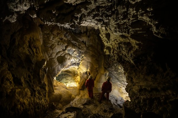 Two people shining their headlamps on the walls of a dark cave during a tour.