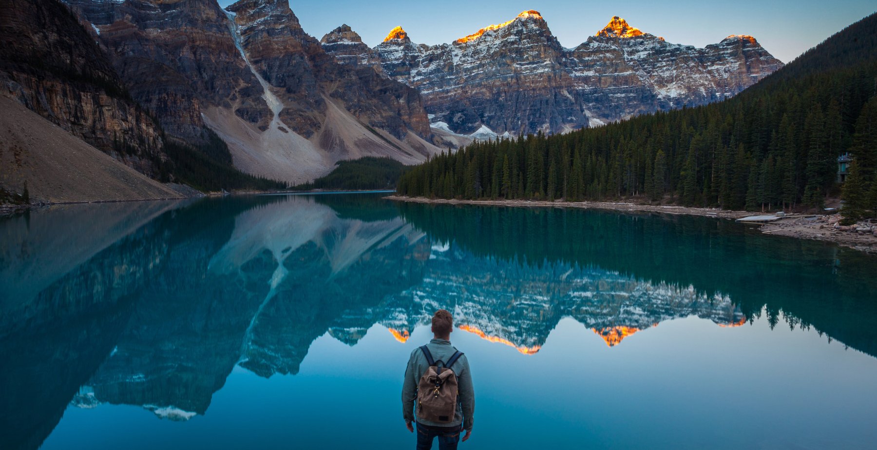 Hiker standing on a rock looking at mountains reflecting in Moraine Lake in Banff National Park