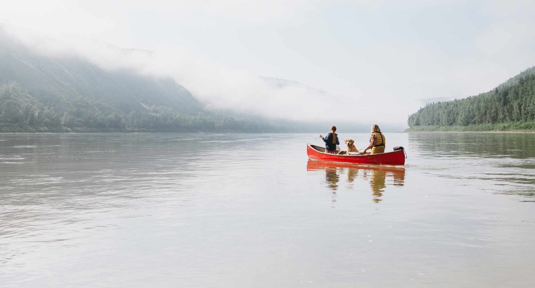 Couple with dog paddling canoe in Peace River