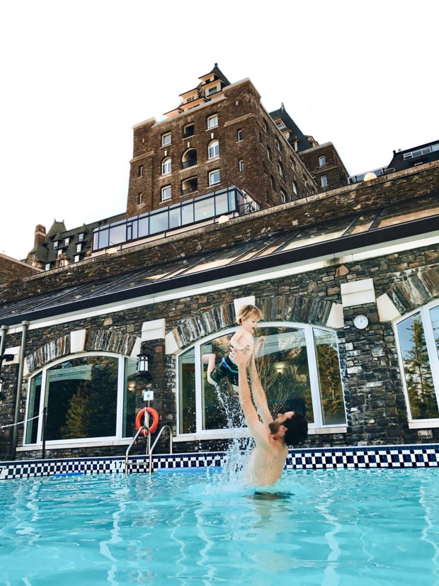 Father tossing his son in the air while in an outdoor pool of a historic hotel.