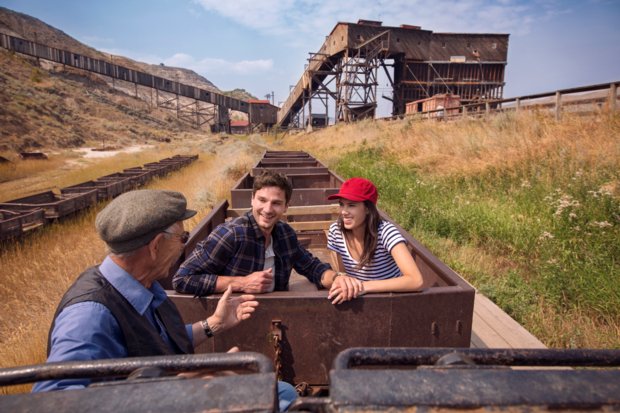 A man and woman chatting and smiling with the tour guide while they ride in an old mine cart at a historic Coal Mine