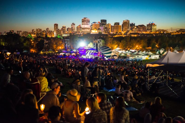 Crowd watching the Edmonton Folk Music Festival with views of the Edmonton cityscape at dusk.