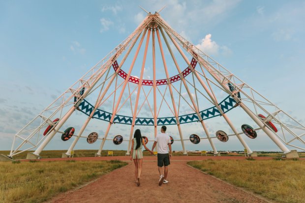 A couple hand in hand walking towards a large tipi made out of metal.
