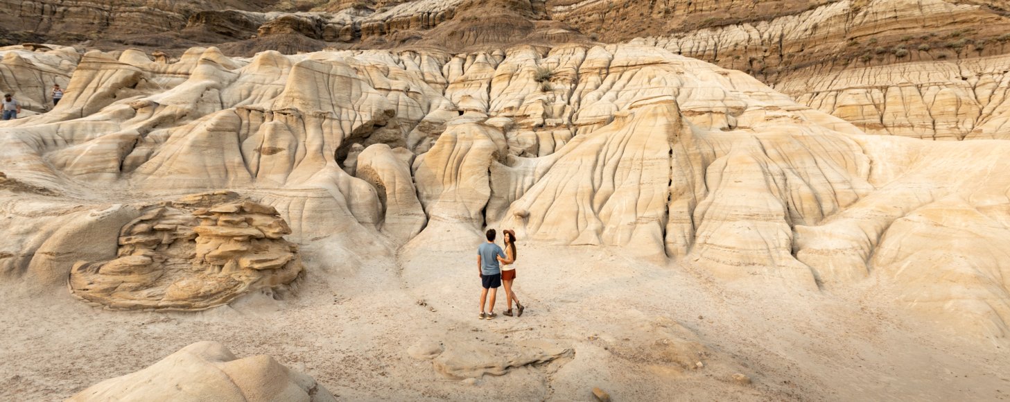 Young couple stand posing fpr a picture beneath the imposing hills of the hoodoo trail Drumheller.