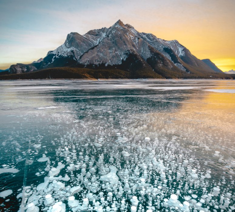 Ice bubbles on a frozen lake with a mountain vista in the background.