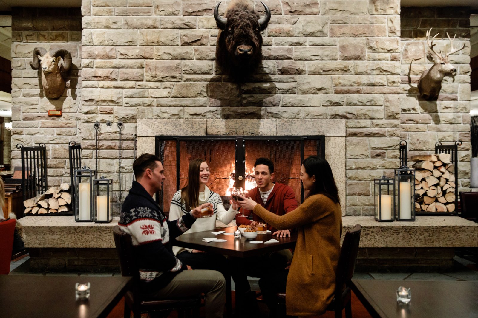 Friends enjoying drinks in front of a rustic fireplace at the Fairmont Jasper Park Lodge.
