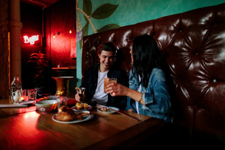 Man and woman smiling and eating dinner and drinking craft cocktails at a restaurant.