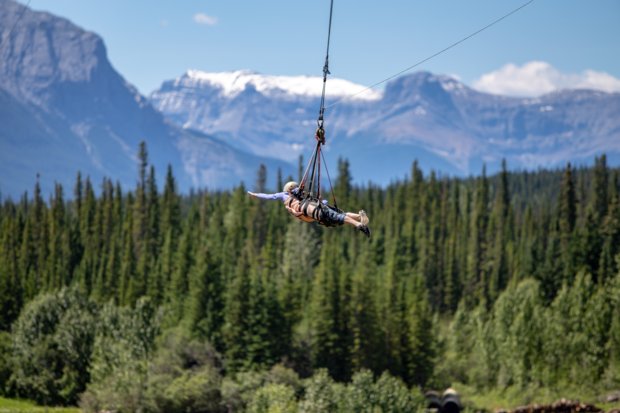 A visitor suspended in the air on their zipline ride with mountains in the background.