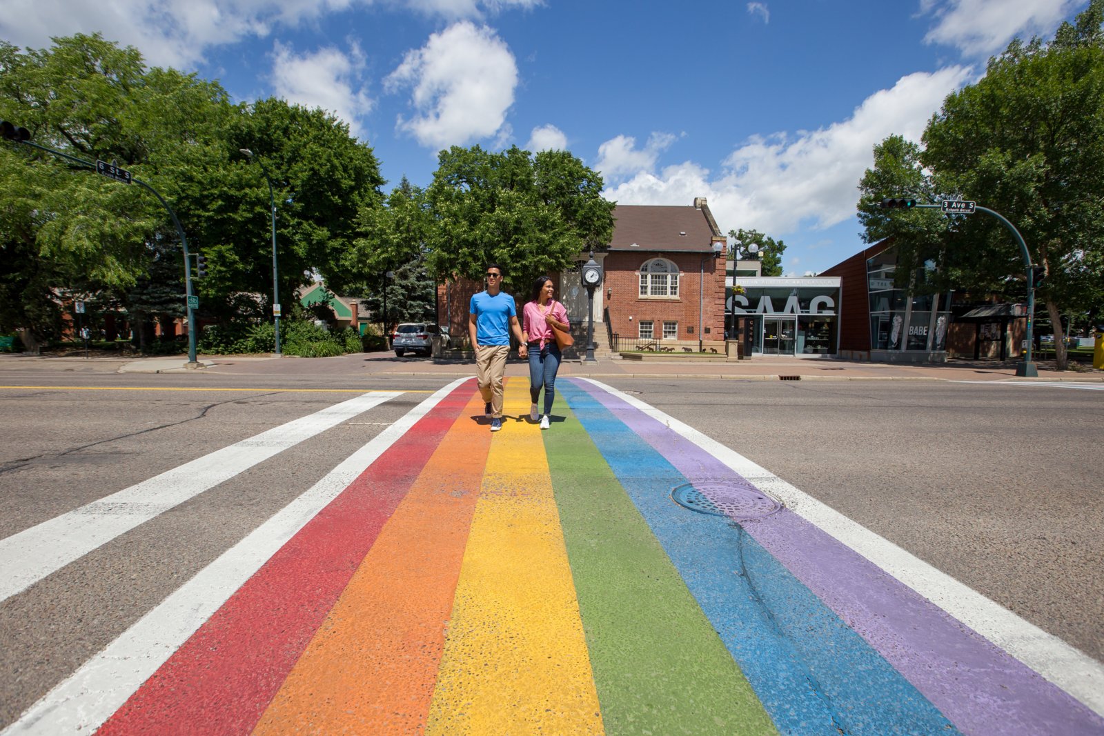 Couple walking hand in hand on a rainbow flag cross walk in downtown Lethbridge.