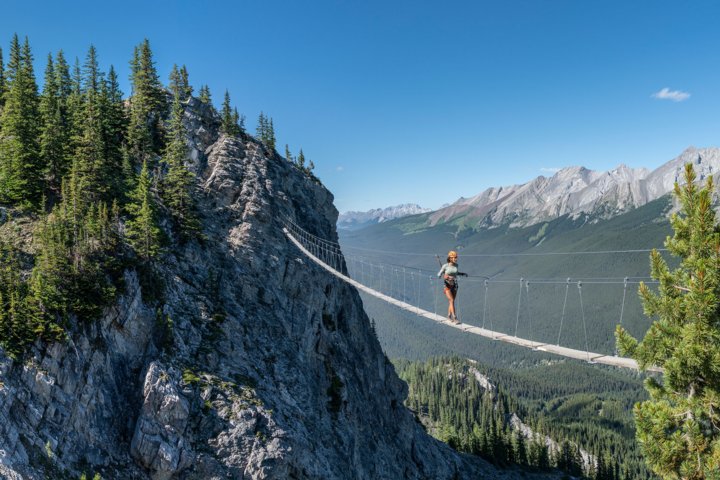A person crosses a long wire bridge between two peaks near Mount Norquay, Banff National Park.