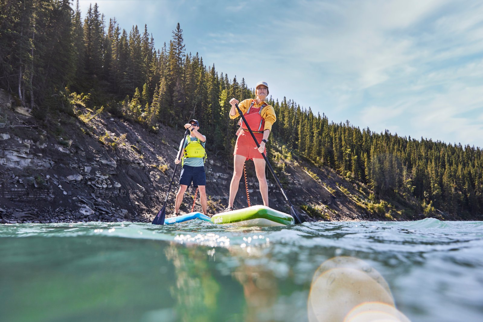 A couple stand up paddle boarding on a river during a hot summers day with a focus on the stream ahead.