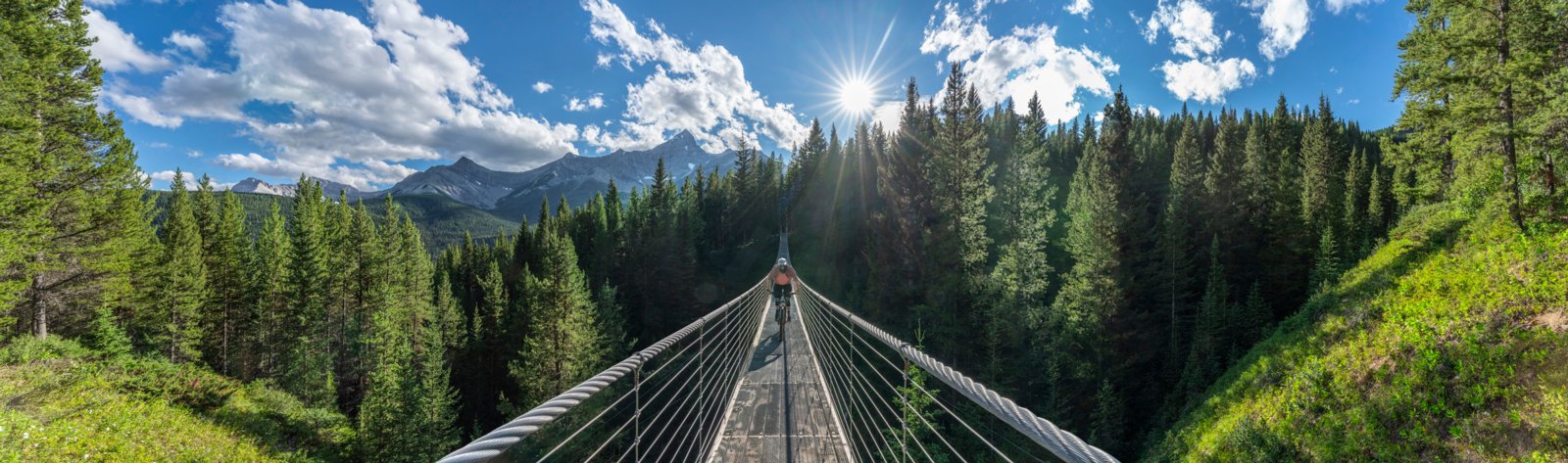 Person on a bike peddling in the middle of the Blackshale Suspension Bridge in Kananaskis Country.