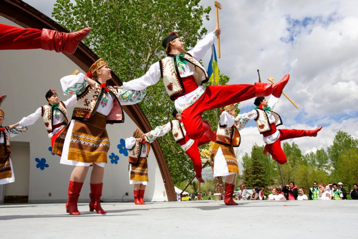 Ukrainian Cultural dancers in uniform preforming on a stage in a park.