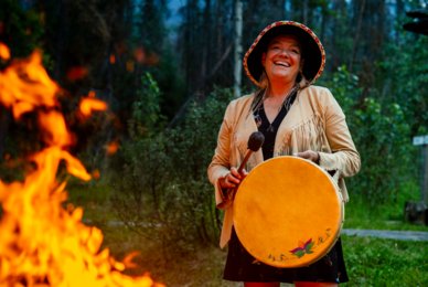 Matricia Brown from Warrior Women striking a drum next to a fire.