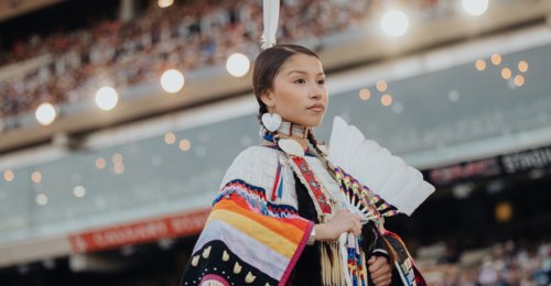 Female Indigenous performer standing in front of a large stadium crowd.
