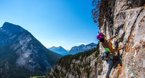 Women rock climbing up the side of a mountain with a river and mountain view in the background