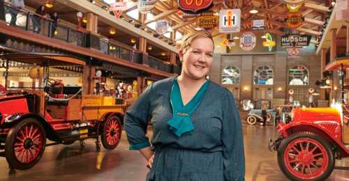 A woman stands in front of vehicles in the Gasoline Alley Museum at Heritage Park Historical Village.
