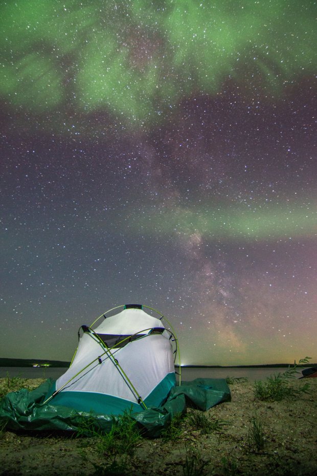 Northern Lights in the nights sky above a camping tent at a lake shore.