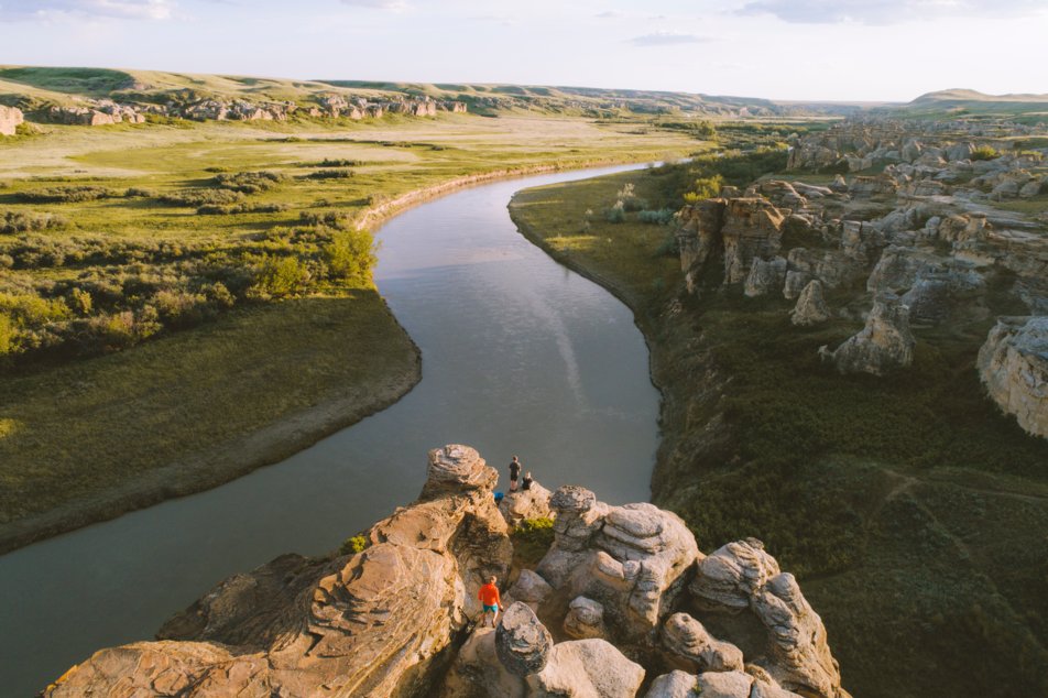 Distance shot of people hiking and standing on hoodoos overlooking a river view