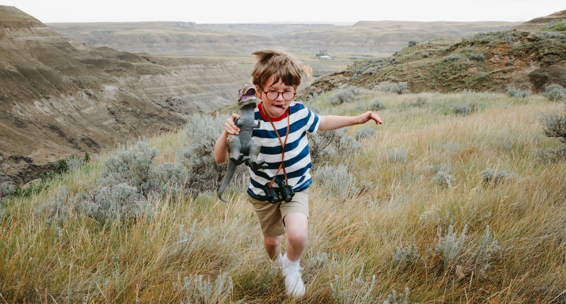 A child running through a meadow in the Canadian Badlands with a dinosaur toy.