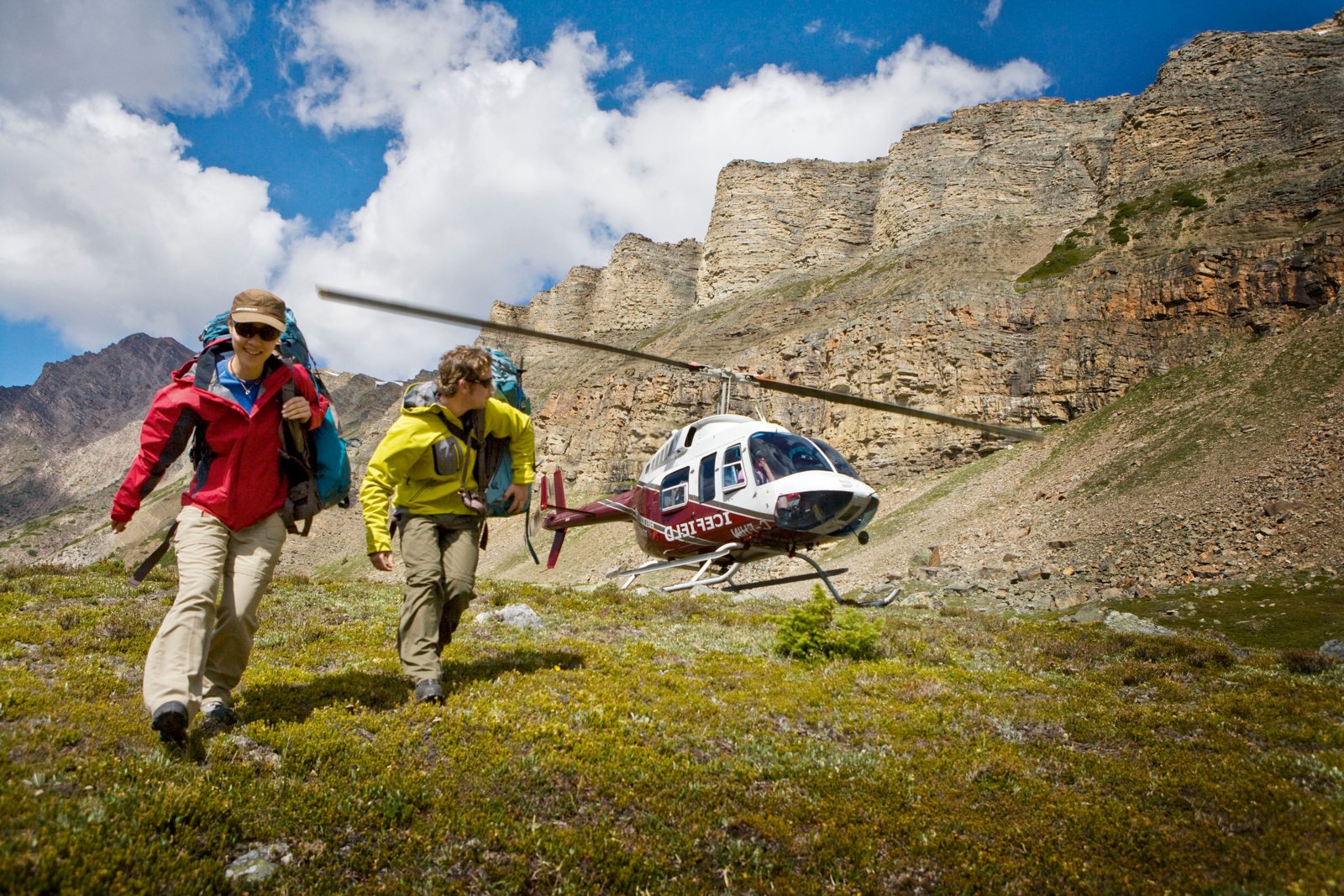 Two people crouched as they walk away from a running helicopter that landed in the alpine of the mountains.