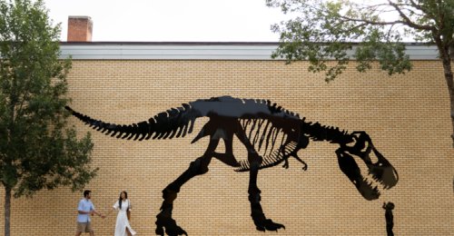 Two people walk past a dinosaur mural in downtown Drumheller.