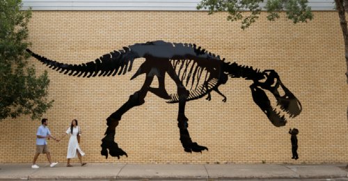 Two people walk past a dinosaur mural in downtown Drumheller.