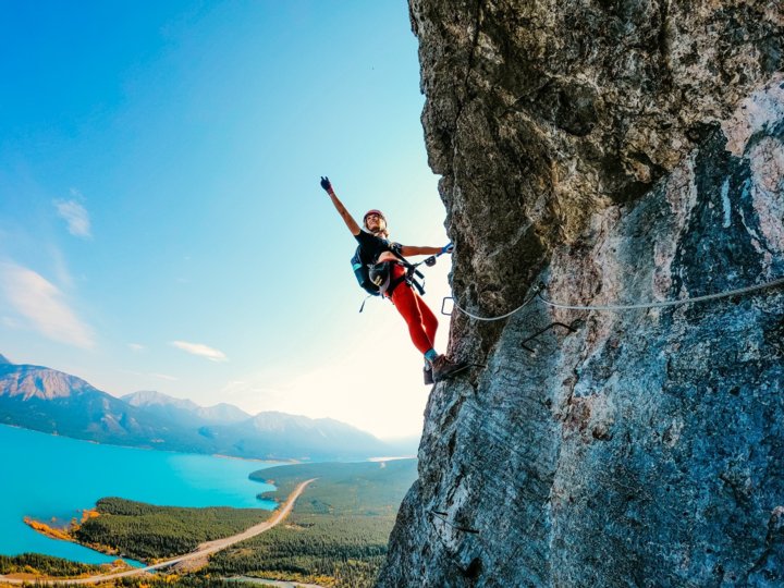 Rock climber waving off the side of a mountain headwall with a lake view in the background