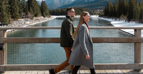 Couple walking along a riverside bridge with mountains in the background