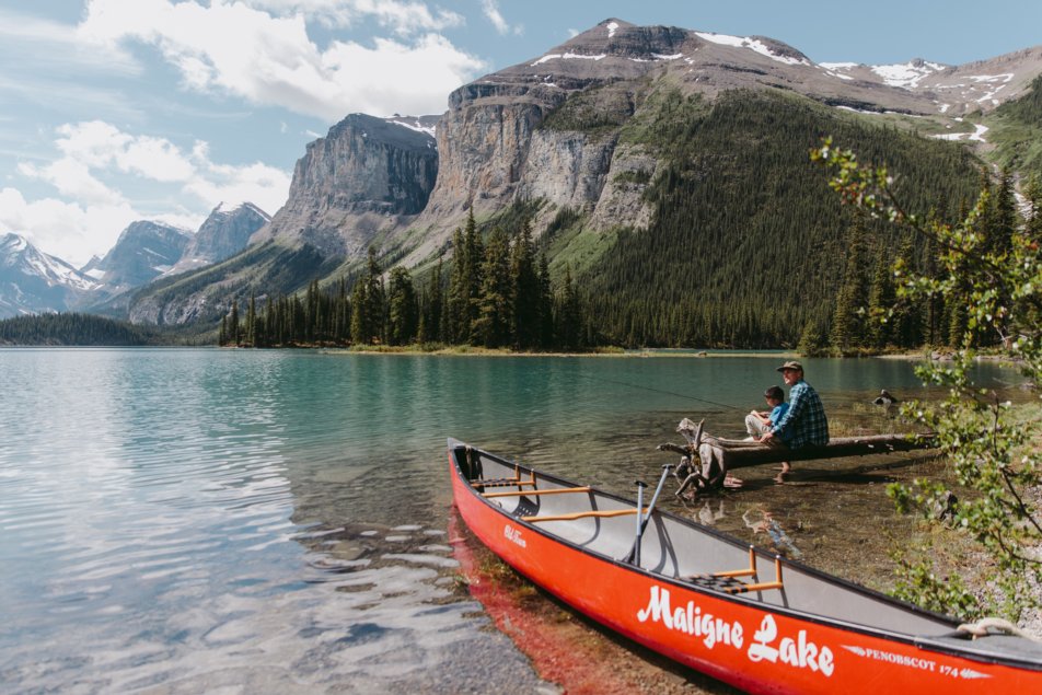 Man and boy fish beside maligne lake and canoe in the Canadian Rocky mountains