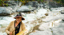 Female Indigenous cree elder from Warrior Women plays a hand drum in front of a river in Jasper National Park.