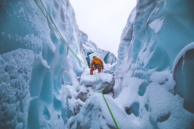 View from below an ice climber making their way through a glacier canyon.