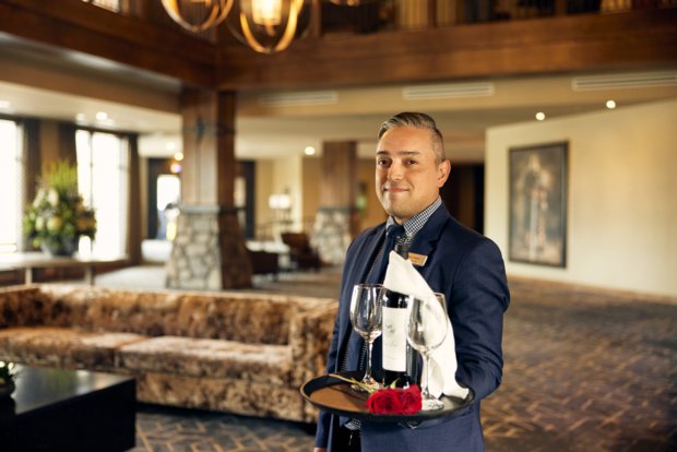 Hotel employee carrying a wine bottle and two wine glasses on a tray with roses.