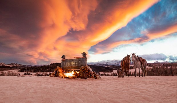 Couple in outdoor rural hot tub in winter with horses in the background and a beautiful sunset.