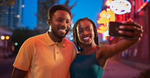 Couple taking a selfie on the street at night with neon signs in the background