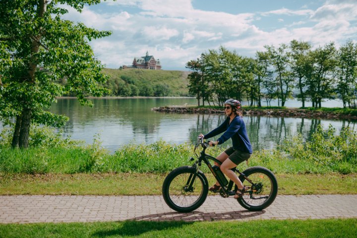 Person riding an ebike on a stone path around a lake with a hotel in the background.