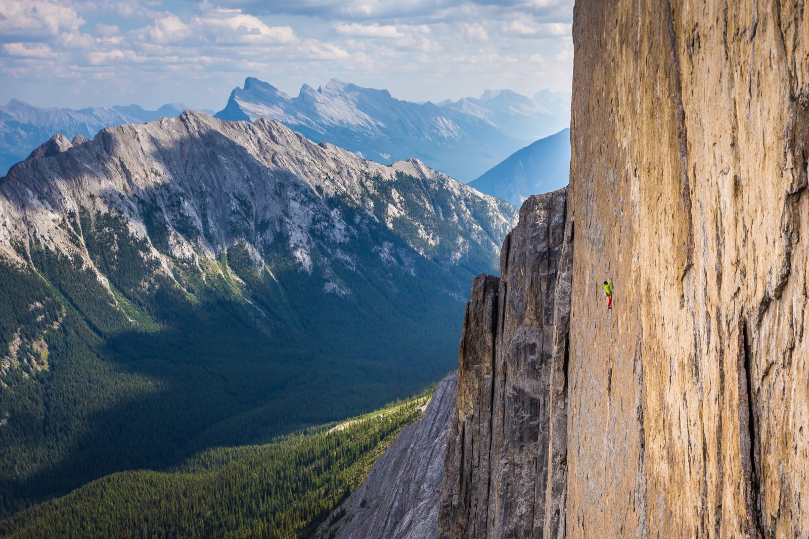 Far away shot of a rock climber of a flat mountain headwall with a mountain view.