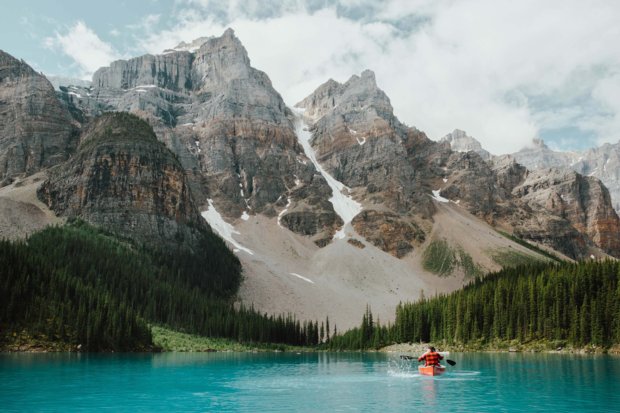 A person paddling a canoe on Moraine Lake surrounded by mountains in Banff National Park.