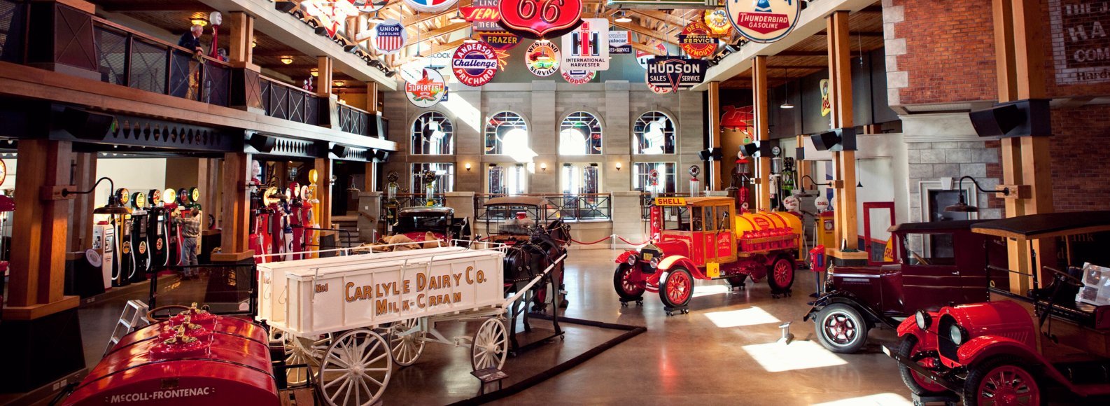 Interior view of a museum filled with old cars and gas station signage.