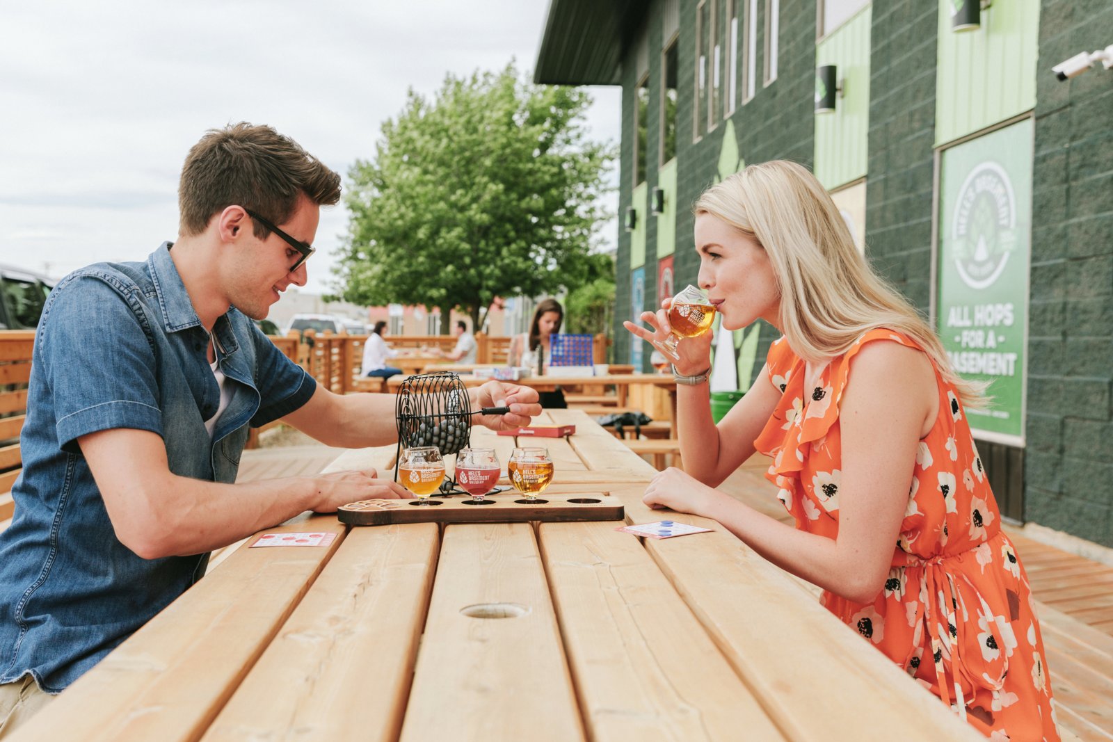 Couple sharing a beer flight at Hell's Basement Brewery's outdoor picnic table.