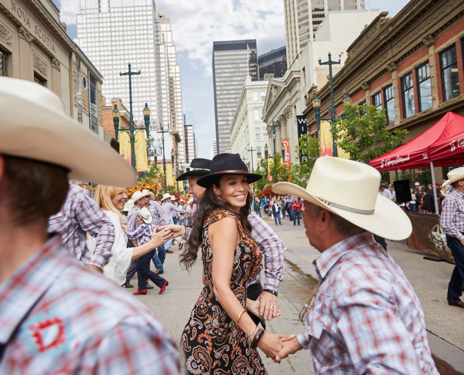 Couple square dancing in downtown Calgary with people and high rises in the background.