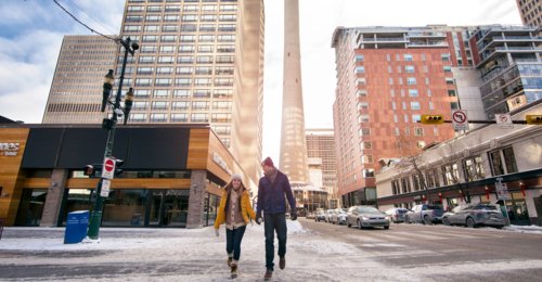 Couple walking down a snowy street in the winter, with the Calgary Tower and downtown buildings in the background